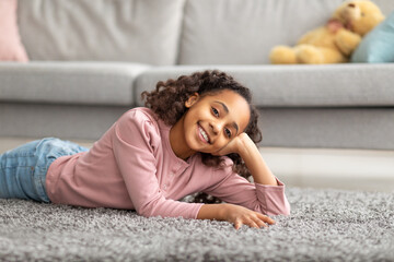Teen's portrait. Positive african american girl smiling to camera, lying on carpet at home