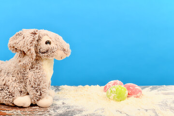 Rabbit on the table with flour and Easter eggs on a blue background.