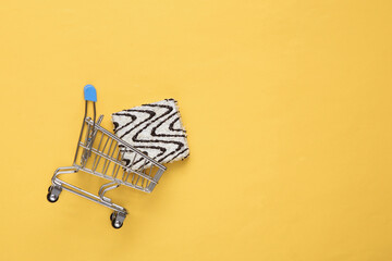 Shopping trolley with delicious cake with frosting on a yellow background