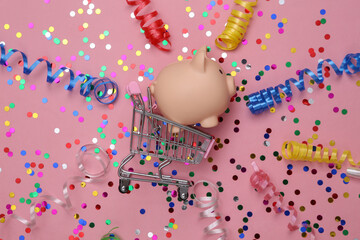 Shopping trolley with piggy bank, Colored streamer and confetti on a pink background. Holiday...