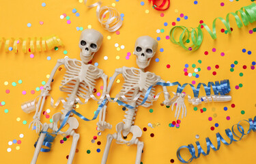 Skeletons with colored streamer and confetti on yellow background. Halloween celebration, fun and fear. Top view. Flat lay