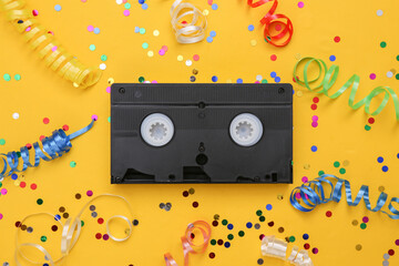 Video cassette and colored streamer with confetti on yellow background. Movie day