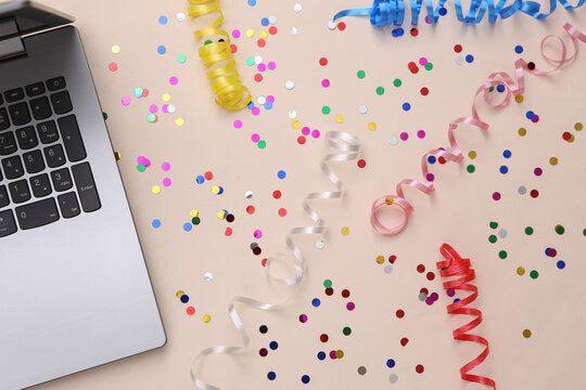 Laptop with Colored streamer and confetti on beige background. Holiday, birthday background