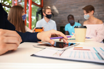 Group of young business people in preventive masks discussing something while working in the creative office