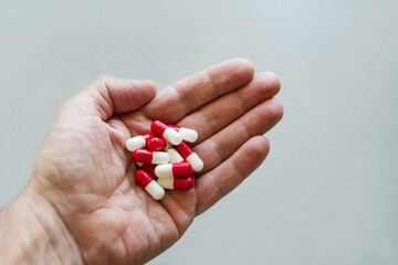 Handful of red and white capsules on the palm of a human hand on a gray background. Medicine....