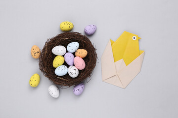 Nest with colored quail eggs and origami chicken on gray background. Easter composition