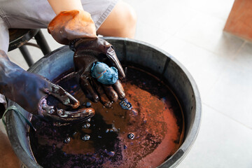 Closeup of hand wearing gloves dying the cotton fabric to indigo color. Process of making cloth from natural cotton wool.
Selective focus with copy space.
Thai and asian culture concept.