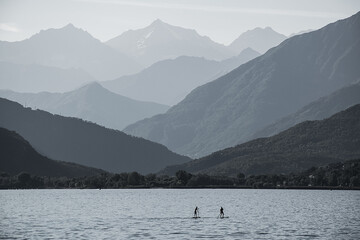 Tourists on SUP in the middle of the vast expanses of Lake Maggiore in Italy against the backdrop of beautiful mountains. The contour lighting creates a halftone perspective.