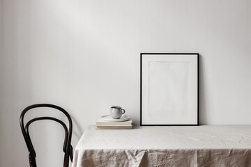 Home office concept. Empty black vertical picture frame mockup. Cup of coffee on old books, linen...