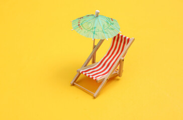 Mini beach deck chair with umbrella on yellow background. Beach vacation, summer time, sunbathing concept