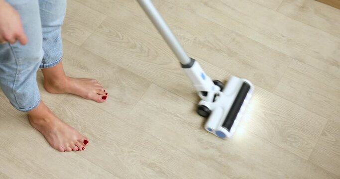 Unrecognizable female using modern vacuum cleaner to remove dust from floor while tidying room at home, woman wife do daily house cleaning routine.