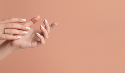 Hands of a beautiful well-groomed woman with feminine nails on a beige background. Manicure, pedicure beauty salon concept. Empty space for text or logo. On nails white gel polish