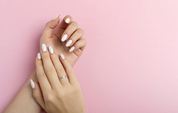 Hands of a beautiful well-groomed woman with feminine nails on a pink background. Manicure, pedicure beauty salon concept. Empty space for text or logo. On nails white gel polish