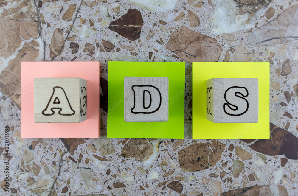 Fototapete ads concept with wooden cubes with alphabet letters arranged on three brightly colored memo pads ove