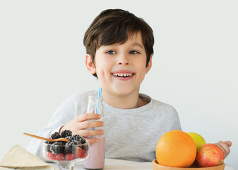 Smiling, laughing boy 6 years old in a gray T-shirt is having breakfast at the table. Cute boy...