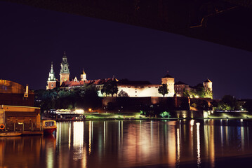 Fototapeta na wymiar Night view on Wawel Castle in Cracow. Beautiful reflections in Wisla river, citylights directed towards the castle.