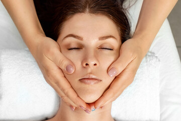 Facial massage close-up. Young, beautiful girl at spa procedures. Skin care, oriental massage treatments, beauty treatments.