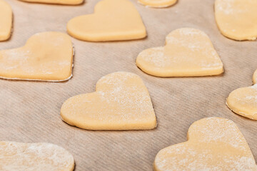 Fototapeta na wymiar Homemade shortbread cookies in the shape of a heart are neatly laid out on parchment in flour. Close-up, top and side view.