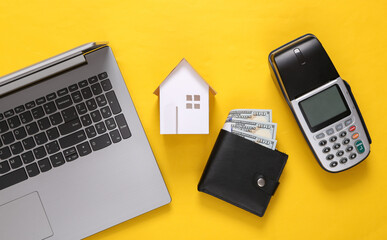 Home buying concept. Laptop, Mini house, payment terminal and purse on yellow background. Top view