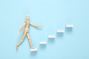 Career growth concept. Wooden puppet climbing up the steps on a blue background