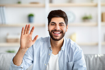 Greeting gesture concept. Happy arab man waving hand to camera, saying hello and laughing