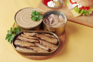 Opened jars with canned fish, sprats and mackerel on a yellow background.