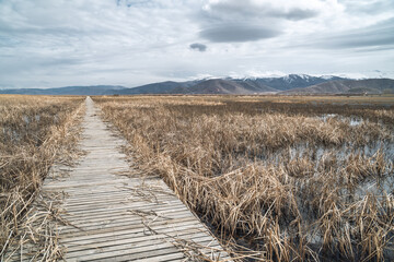 Moody panoramic view of bridge over a lake with marshes and snow-capped mountains in the background in Sultan Reedy National Park, central Turkey on a cloudy day