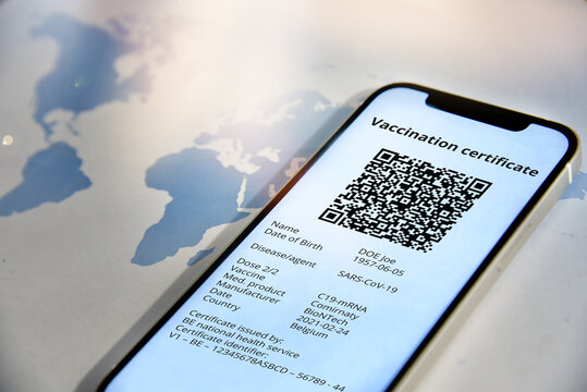 Travel and tourism concept during coronavirus pandemic. Smartphone with digital certificate of vaccination against Covid-19 in front of the world map.