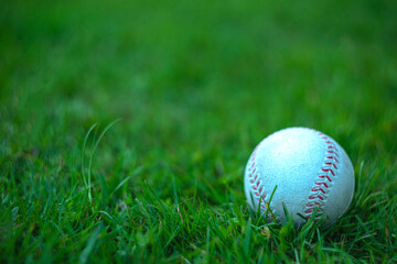 White baseball ball on green grass, artistically blurred background with bokeh