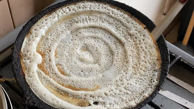 Folding Dosa to eat, a South Indian traditional breakfast meal in a hot frying pan with a flat spoon - Indian Cuisine