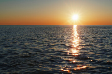 Fototapeta premium A sunny sunset on the sea stretching into the horizon with a path and highlights on the sea.