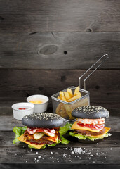 Two burgers with fries served with souces on wooden table