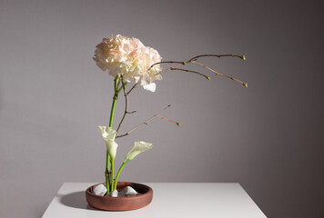 Flower arrangement of hydrangea, calla lilies and tree branches in clay vase with white stones....