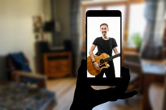 Watching online concert at home. Singer with a guitar on the screen of the smartphone