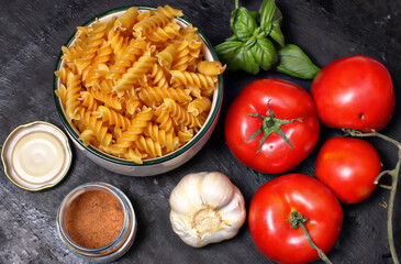 Ingredienti crudi per un buon piatto di pasta alla mediterranea. Fusilli, pomodori, aglio,basilico e spezie su fondale scuro.
