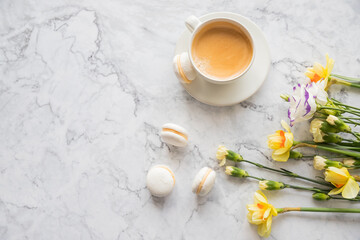 Macaroons with white cup of coffee, bright beautiful flowers on marble background.Beautiful breakfast for woman. Spring concept.Copy space