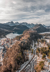Aerial drone shot of Hohenschwangau by lake in Fussen with view of Alps snow mountain range in Germany winter