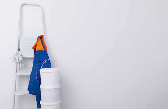 three buckets of paint on top of each other, a white ladder and a protective jacket for the master, there is a place for writing on the white wall