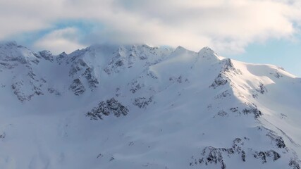 Amazing ancient mountains with high sharp peaks covered with snow under blue sky with soft clouds in winter morning aerial view