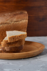 slices of black bread on a wooden tray with a loaf of bread in the background