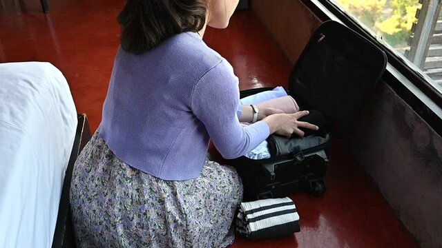 Footage video of young Asian woman opening her suitcase for pack and arranging clothing before traveling in her holiday period.