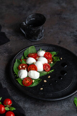 Caprese salad with mozzarella, tomatoes and basil on a black plate. Food styling