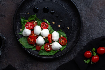 Caprese salad with mozzarella, tomatoes and basil on a black plate. Food styling