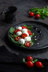 Caprese salad with mozzarella, tomatoes and basil on a black plate. Food styling