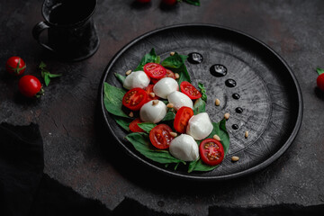 Caprese salad with mozzarella, tomatoes and basil on a black plate. Food styling