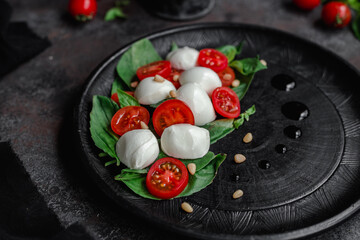Caprese salad with mozzarella, tomatoes and basil on a black plate. Food styling