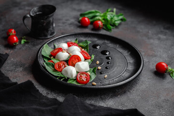 Caprese salad with mozzarella, tomatoes and basil on a black plate. Food styling