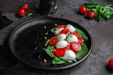 Caprese salad with mozzarella, tomatoes and basil on a black plate. Food styling