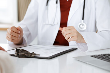 Unknown woman-doctor and patient discussing something while sitting at the table in clinic, close-up. Medicine concept