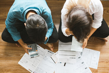 Top view asian couple sitting on the floor stressed and confused by calculate expense from invoice or bill, have no money to pay think of take the house to mortgage causing debt, bankruptcy concept.